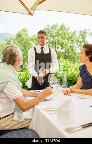 Sommelier che mostra la bottiglia di vino per accoppiare i pasti presso il patio tabella Foto Stock