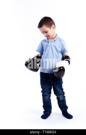 Un ragazzino con i capelli scuri in jeans blu, azzurro polo in bianco e nero guantoni da pugilato si diverte, pugilato e considera se stesso un vincitore su Foto Stock