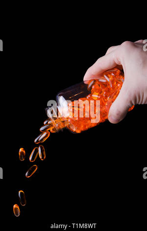 Colata a mano una bottiglia di medicina arancione capsule contro sfondo blu Foto Stock