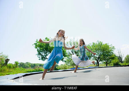 Giocoso e spensierato a piedi nudi ragazze in abiti giocando sul trampolino nel cortile soleggiato Foto Stock