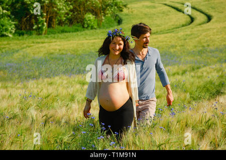 Ritratto felice coppia incinta camminando in soleggiato, idilliaco campo rurale con fiori selvatici Foto Stock