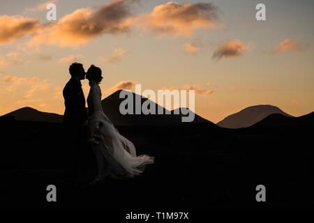 Silhouette sposa e sposo che si baciano al tramonto con montagne tranquille sullo sfondo Foto Stock