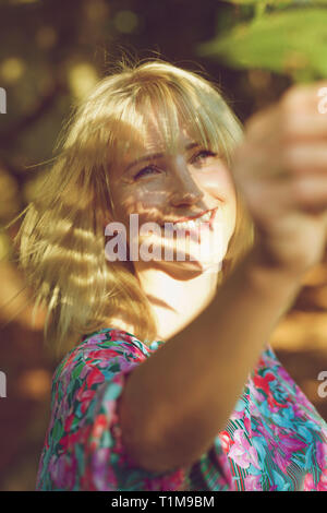 Carefree donna raggiungendo per leaf Foto Stock