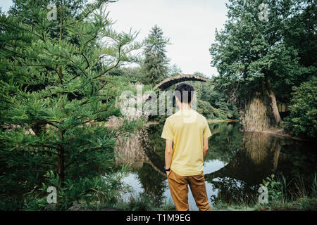 Ragazzo adolescente che guarda il tranquillo Rakotzbruecke Devils Bridge, Rakotzbruecke, Brandeburgo, Germania Foto Stock