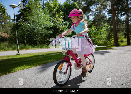 Carino bambina bicicletta equitazione. Felice active kid. Giorno d'estate e di sole sul sobborgo street. Foto Stock