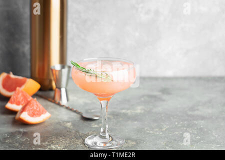 Estivo rinfrescante cocktail champagne di pompelmo succhi di rosmarino in calici in vetro su una luce di cemento grigio Sfondo. Foto Stock