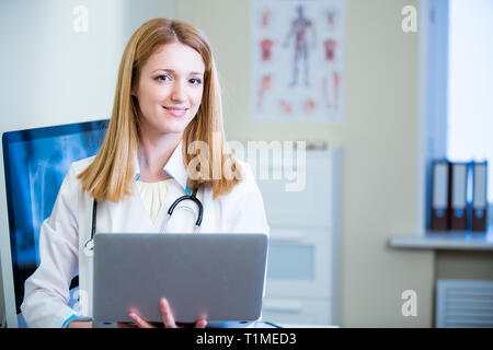 Ritratto di medico femminile amichevole e sicuro in ospedale lavorando su laptop. Personale medico entusiasta al lavoro. Medico femminile nella sala diagnostica. Foto Stock