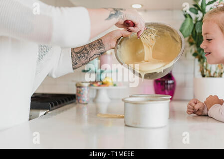 Figlia che guarda la madre con tatuaggi cottura in cucina Foto Stock