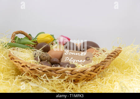 Joyeuses Pâques è felice Pasqua scritto in francese su una etichetta in un cesto di vimini riempito con uova e tulipani Foto Stock
