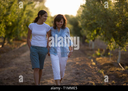 Una madre e il suo cresciuti figlia a piedi attraverso un frutteto Foto Stock