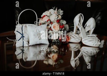 Bouquet nuziale, gli anelli di nozze, le scarpe della sposa si riflettono sul tavolo di vetro. Foto Stock