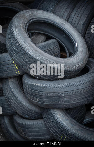 Pila casuale di auto usate di pneumatici impilati per la rivendita in un centro di distribuzione Foto Stock