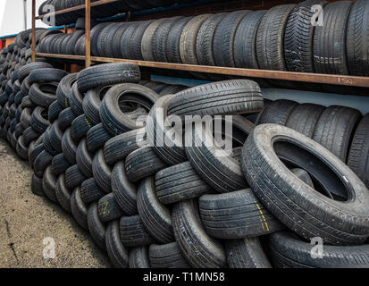 Neat cremagliere di auto usate di pneumatici impilati e pronti per il riciclaggio in corrispondenza di un centro di distribuzione Foto Stock