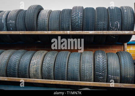 Neat cremagliere di auto usate di pneumatici impilati e pronti per il riciclaggio in corrispondenza di un centro di distribuzione Foto Stock