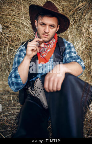 Cowboy rilassarsi con sigaro, pagliaio sullo sfondo Foto Stock