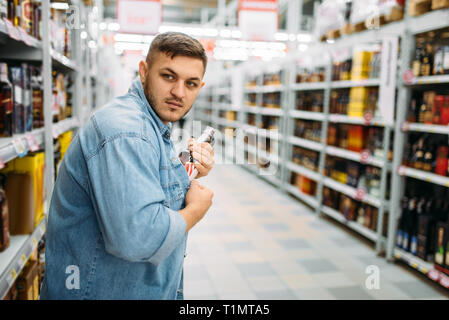 L uomo si nasconde una bottiglia di alcool sotto la sua maglietta Foto Stock