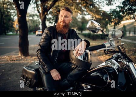 Biker seduto a terra contro il suo trinciapaglia Foto Stock