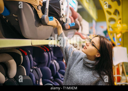 Donna incinta scegliendo seggiolino da bambino per auto in negozio Foto Stock