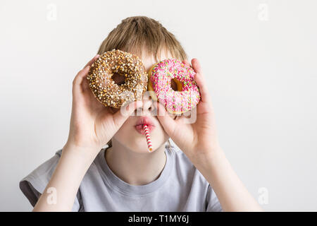 Teen boy guarda nella ciambella fori e smorfie divertenti. Foto Stock