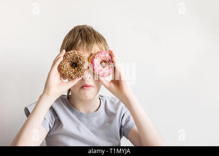 Teen boy guarda nella ciambella fori e smorfie divertenti. Foto Stock