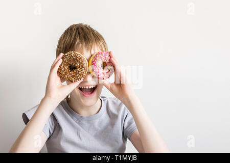 Teen boy guarda nella ciambella fori e sorrisi di divertimento. Foto Stock