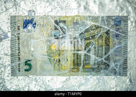5 di banconote in euro congelati in un blocco di ghiaccio. Concetto di capitale bloccato e la crisi finanziaria. Foto Stock