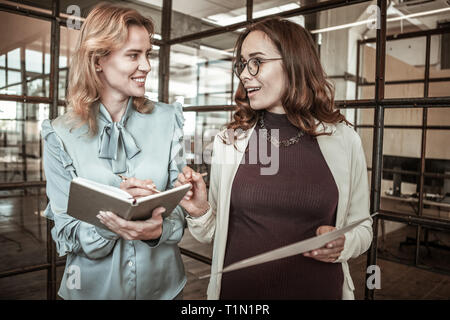Dai capelli scuri raggiante signora in vetri trasparenti aventi conversazione attiva Foto Stock