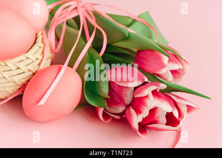 Pasqua composizione fatta con le uova nel paniere pastello su sfondo rosa decorato con tulipani. Biglietto di auguri. Foto Stock