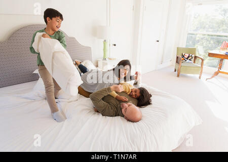 La famiglia felice di combattimento di cuscini sul letto Foto Stock