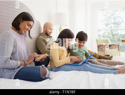 La famiglia utilizzando la tecnologia sul letto Foto Stock