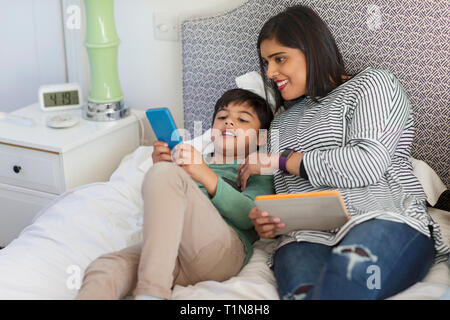 Madre e figlio utilizzando smart phone e tavoletta digitale sul letto Foto Stock