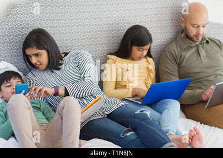 La famiglia utilizzando la tecnologia sul letto Foto Stock