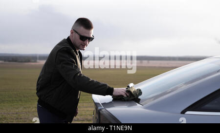Colpo di giovane uomo bello in occhiali da sole la lucidatura della sua auto con un panno Foto Stock