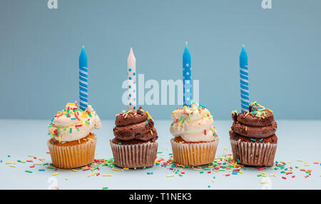 Tortini di compleanno sul pastello blu sullo sfondo. Quattro i tortini di vaniglia e cioccolato con candele di blu Foto Stock