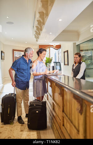 Coppia matura con le valigie il check in presso la reception dell'hotel Foto Stock