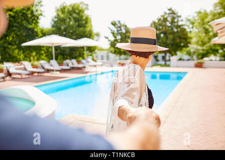 Coppia matura tenendo le mani al sole a bordo piscina Foto Stock