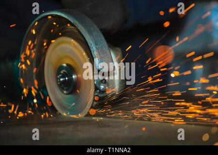 Close-up della rotazione del disco smerigliatrice angolare durante il funzionamento. Scintille luminose dal taglio di metallo. Dark background industriale Foto Stock