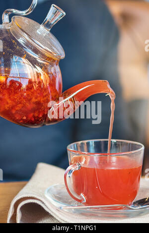 Processo di preparazione del tè, una tazza del preparato di fresco tè di frutta di frutta rossa e il miele. Il tè caldo si riversa dal bollitore nella coppa. Foto Stock