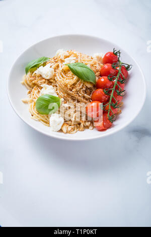 Vegetariano facile italiano piatto di pasta con gli spaghetti, pangrattato, arrosti di vigna di pomodori ciliegia, di foglie di basilico fresco e pezzi di mozzarella in una profonda Foto Stock