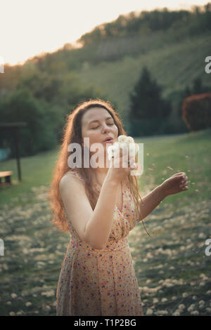 Bella giovane donna soffia un dente di leone Foto Stock