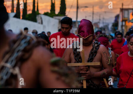 Un cattolico con cappuccio, penitente indossando le catene e le spine di cactus bloccato al suo corpo, prende parte alla Settimana Santa processione in Atlixco, Messico. Foto Stock