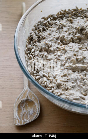 Pasta madre di pasta di pane materie con i semi di girasole in una ciotola di vetro sulla parte superiore della cucina con il cucchiaio di legno. Messa a fuoco selettiva. Foto Stock