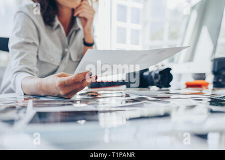 Donna occupato a lavorare nel suo studio. Tagliate il colpo di una femmina di fotografo stampe di controllo dopo lo sviluppo. Foto Stock