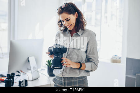 Fotografo femmina controllo foto sulla fotocamera e sorridente. La donna caucasica in casuals in piedi nel suo ufficio guardando le foto sul suo dslr camer Foto Stock
