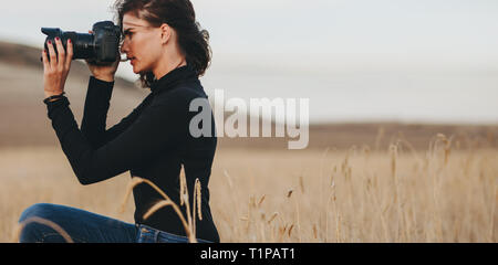 Donna con fotocamera DSLR a fotografare all'esterno. Femmina caucasica fotografo con la fotocamera per scattare foto. Foto Stock