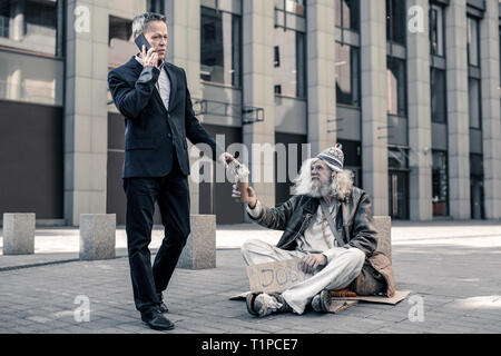 Grati grey-haired senzatetto senior alla ricerca sull'uomo di affari Foto Stock