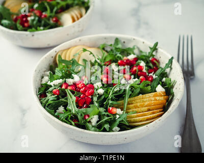 Insalata fresca con rucola, pera, melograno e noce di cocco crumble o ricotta. Due ciotole con deliziosa estate insalata di frutta sulla tavola di marmo. Copia spazio per il testo Foto Stock