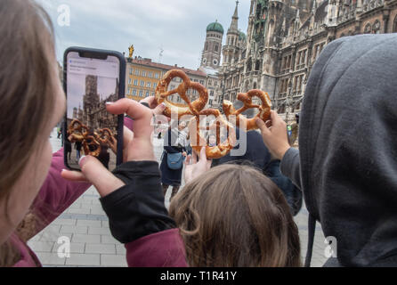 27 marzo 2019, il Land della Baviera, München: Tre turisti fotografare la loro pretzel in Marienplatz nel centro della bavarese capitale dello stato contro lo sfondo del municipio (r) e la Frauenkirche dietro di esso. Foto: Peter Kneffel/dpa Foto Stock