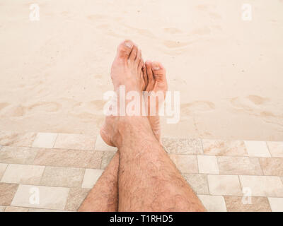 L uomo è rilassante a piedi nudi sulla spiaggia. Primo piano le gambe di Asia uomo di pelle e uomini gambe pelose su sfondo sabbia. Ragazzo gambe sulla sabbia. Foto Stock