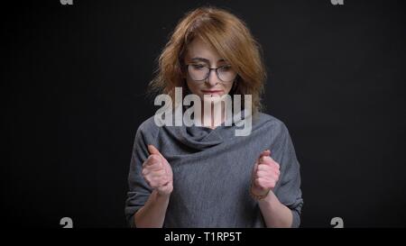 Closeup ritratto di mezza età stravagante redhead femmina in bicchieri di essere preoccupato e nervoso clenching suoi pugni nella parte anteriore della fotocamera Foto Stock